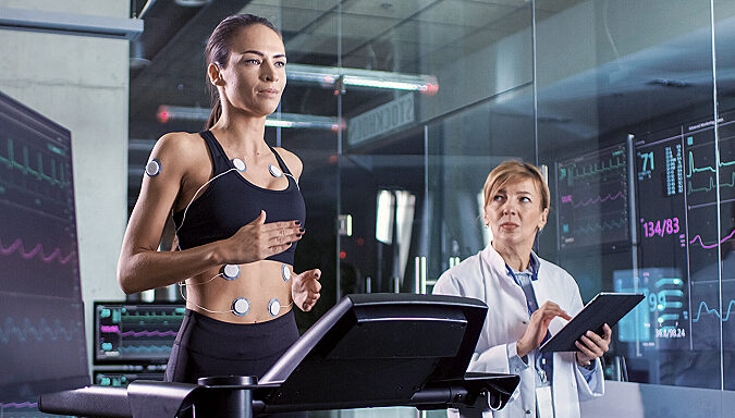 Athlete undergoing a performance and cardiac test on a treadmill with body sensors while a sports scientist monitors the data.