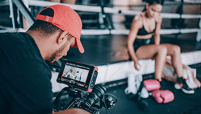 Videographer filming a female boxer at ringside on a camera monitor, representing sports media production.