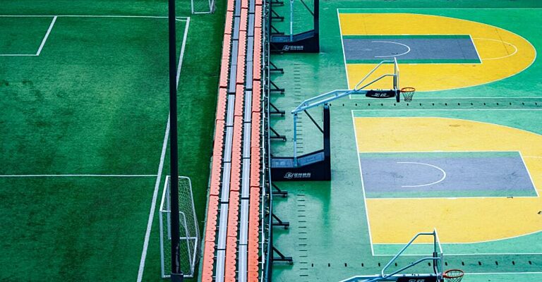 Aerial view of adjacent sports facilities — a green football pitch beside multiple basketball courts — representing sport as a multidimensional economic platform.