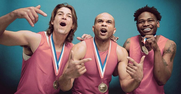 Three athletes in pink jerseys wearing medals, celebrating together against a teal backdrop.