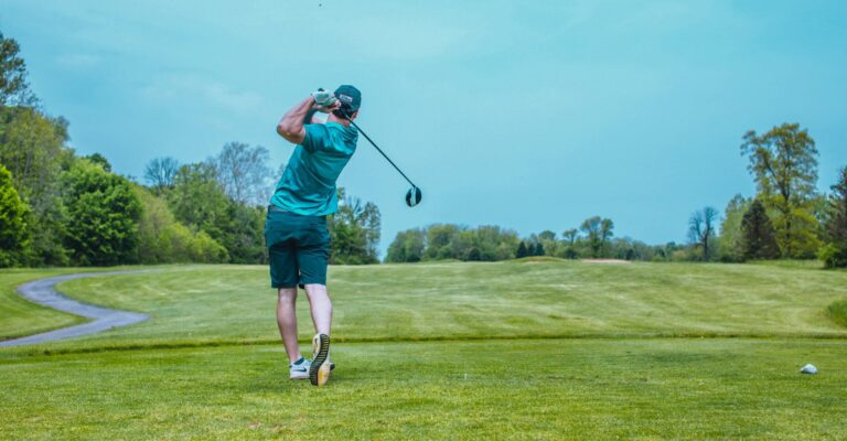 Golfer at the top of the backswing on a green fairway under a bright sky, representing precision and focus.