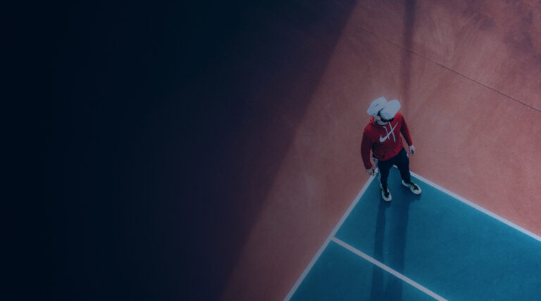 Aerial view of an athlete in a red hoodie wearing a VR headset on a blue-and-orange court, representing the digital future of sport.
