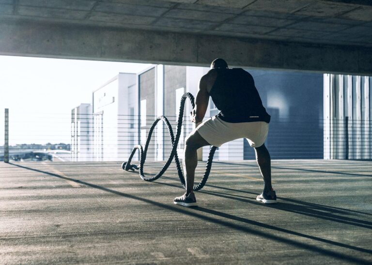 Athlete performing a battle-rope workout in an open concrete parking structure at sunrise.