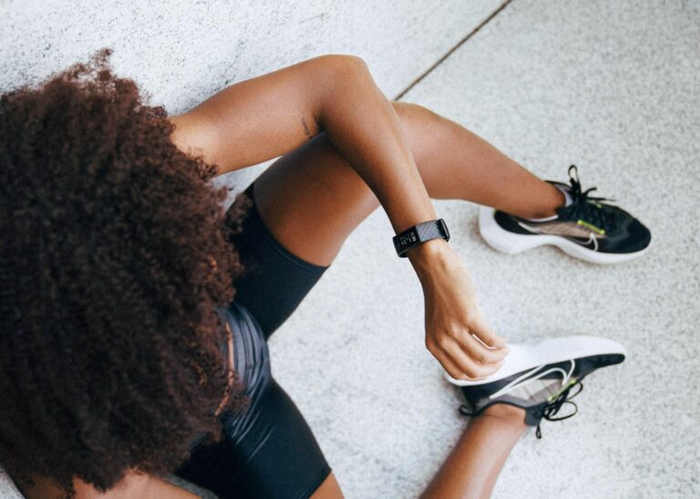 Overhead view of a female athlete in activewear resting on the floor and checking her fitness tracker, wearing running shoes.